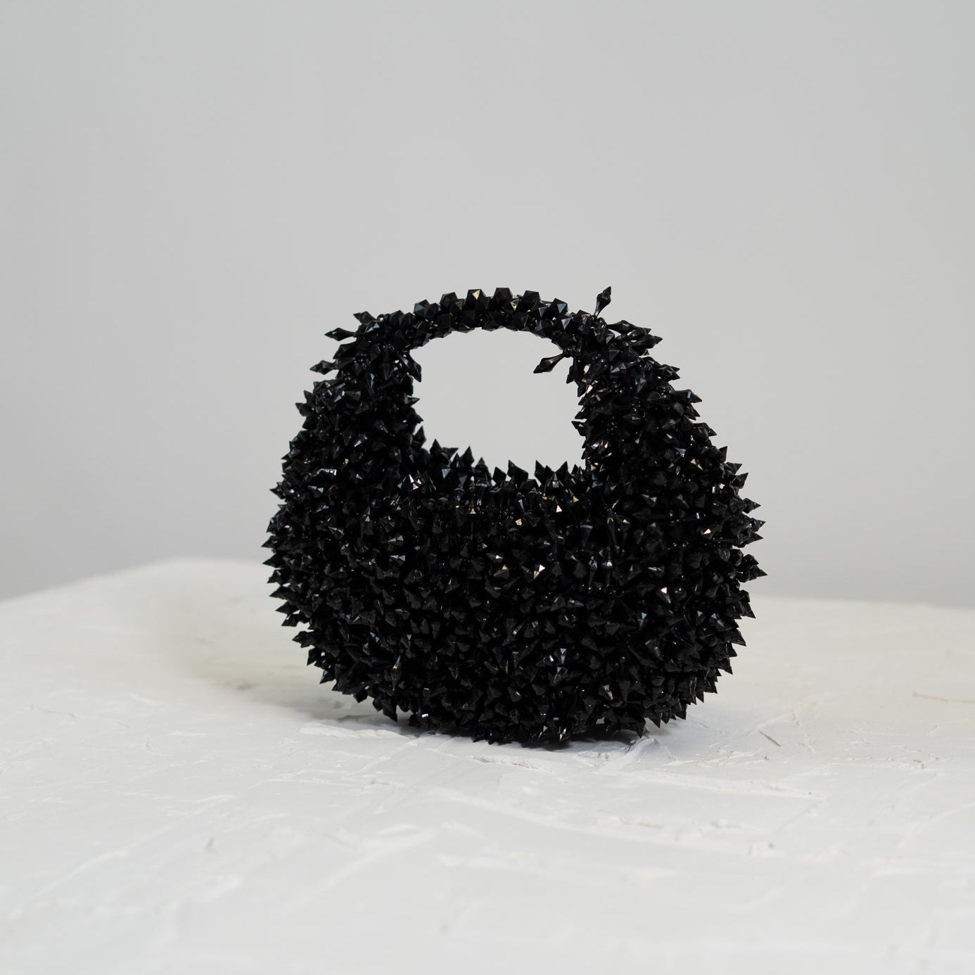 Black textured handbag on a white surface with a light gray background