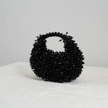 Black textured handbag on a white surface with a light gray background