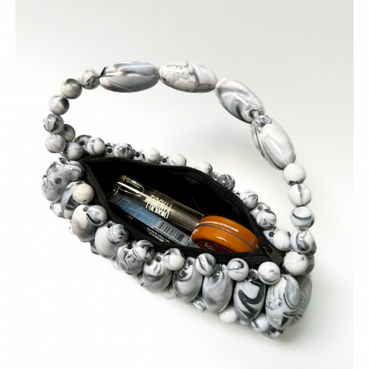 Close up of inside handmade beaded bag in frosted stone - black, white marble swirled tones - showing lip gloss, vaseline, perfume, what can fit inside the black zip pouch