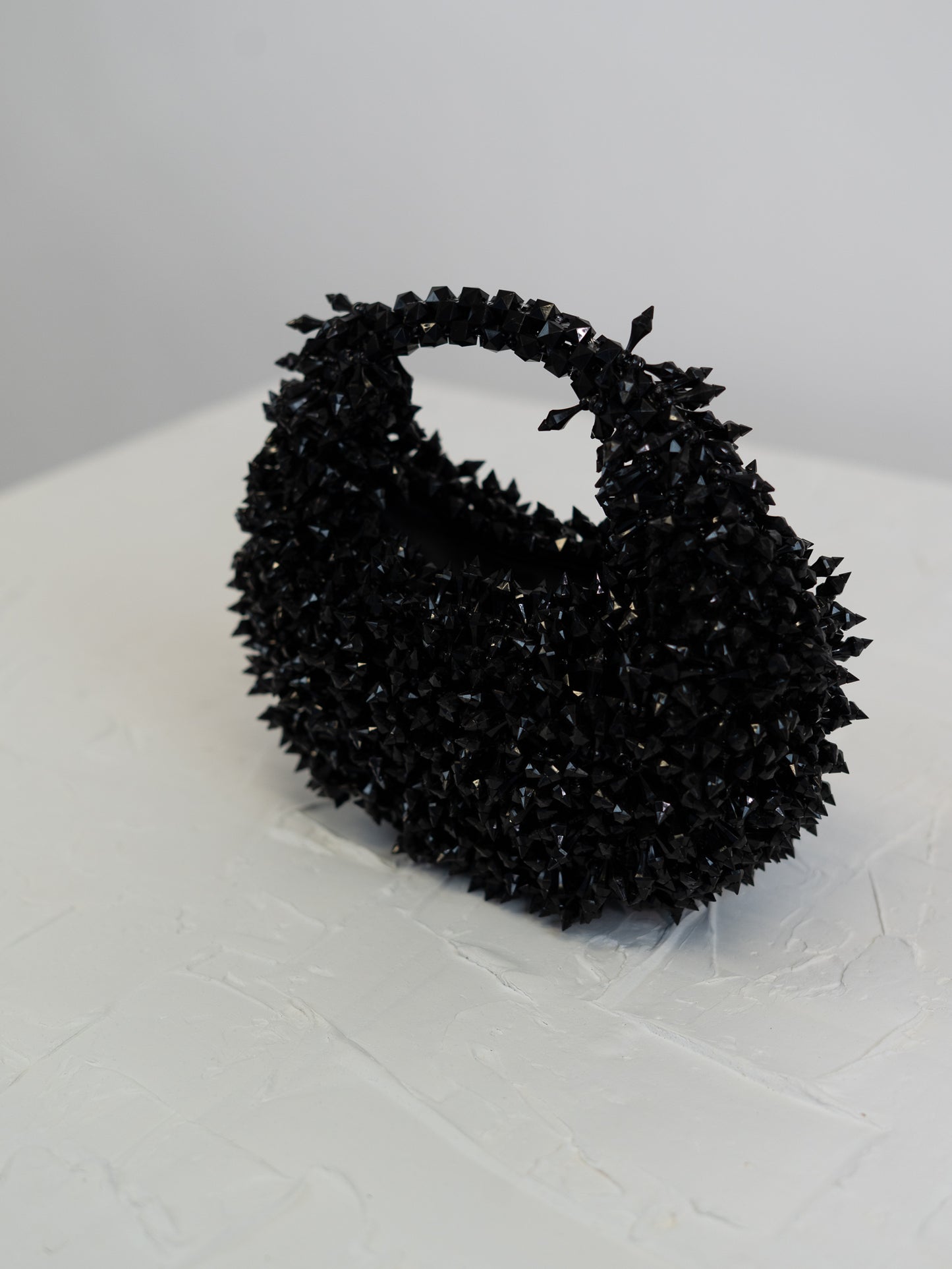 Black textured handbag on a white surface with a light gray background