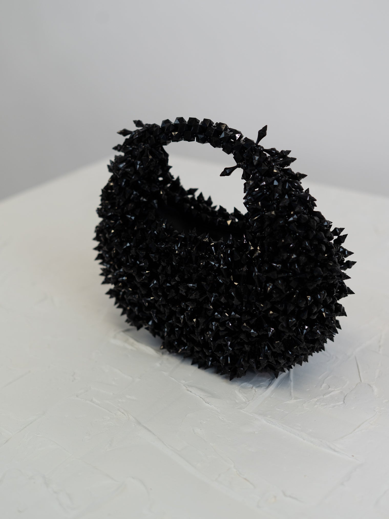 Black textured handbag on a white surface with a light gray background