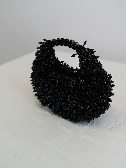 Black textured handbag on a white surface with a light gray background