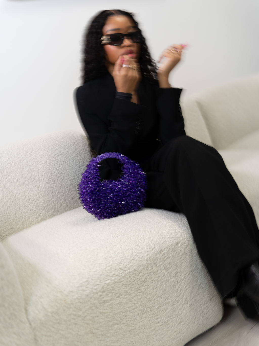 Model applying lip gloss on a couch with the Spiky Purple handmade beaded bag