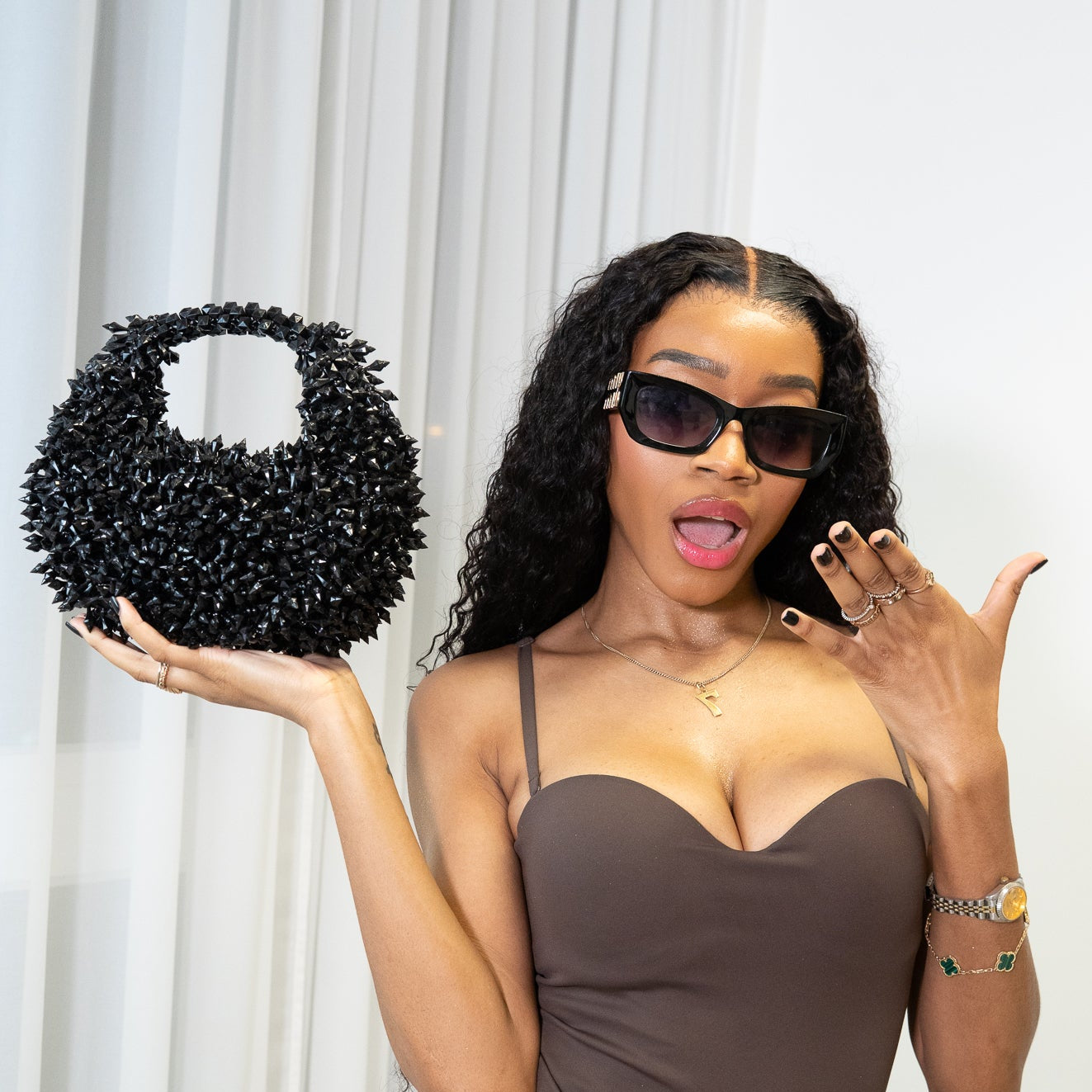 Woman holding a black beaded handbag and wearing sunglasses indoors.