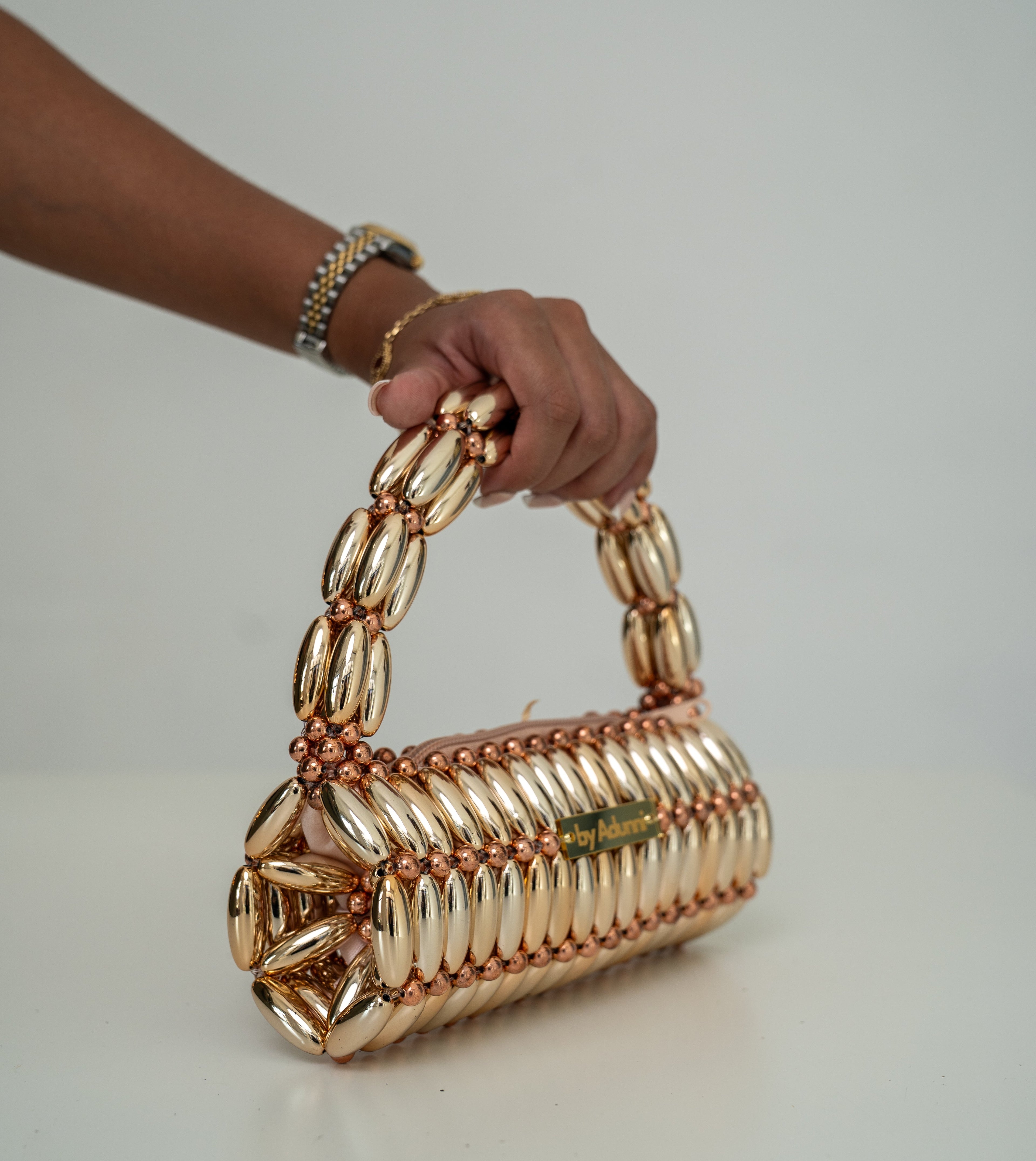 A hand holding a metallic gold chain-link handbag with a matching chain handle, set against a plain light gray background.