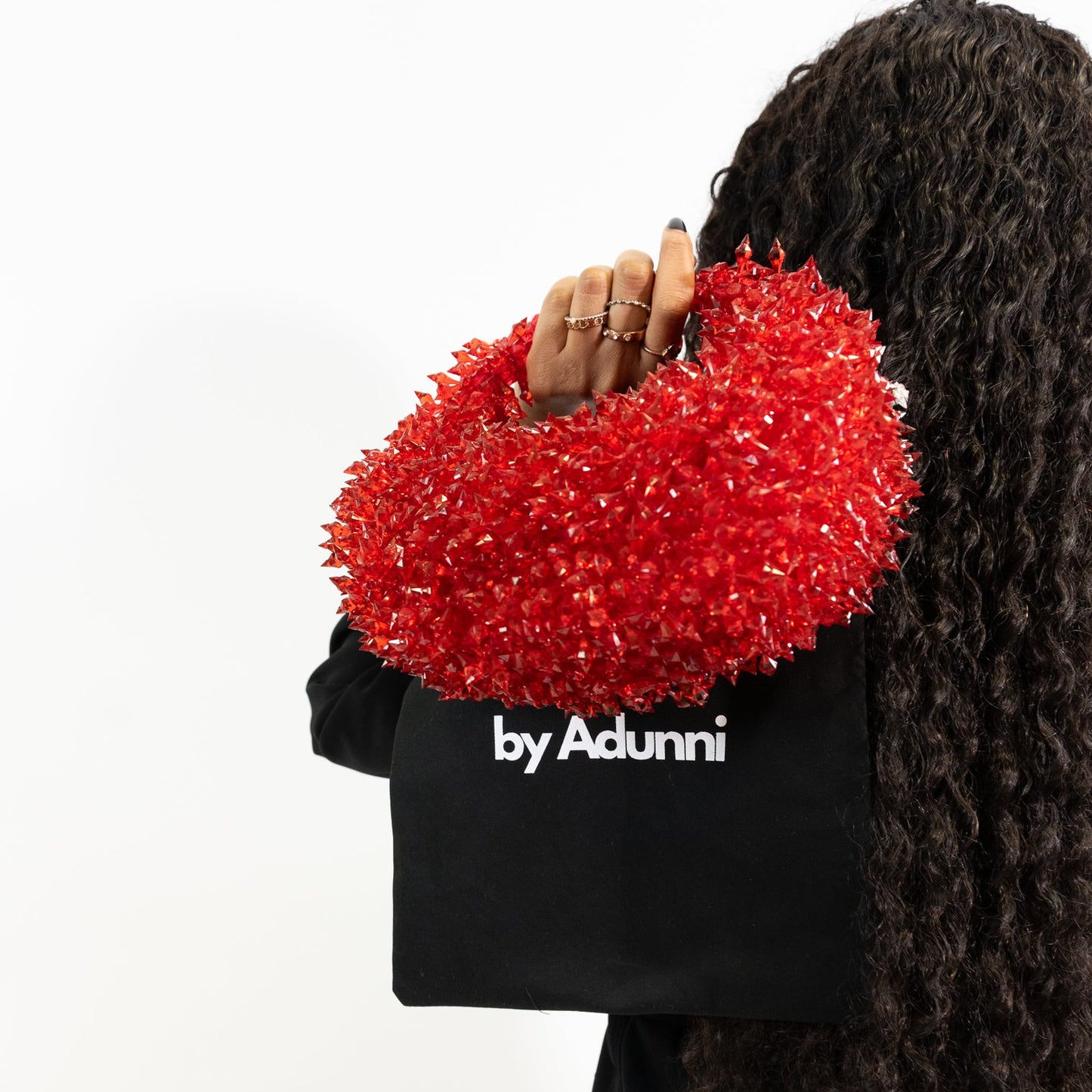 Person holding a red textured handbag with 'by Adunni' branding on a white background