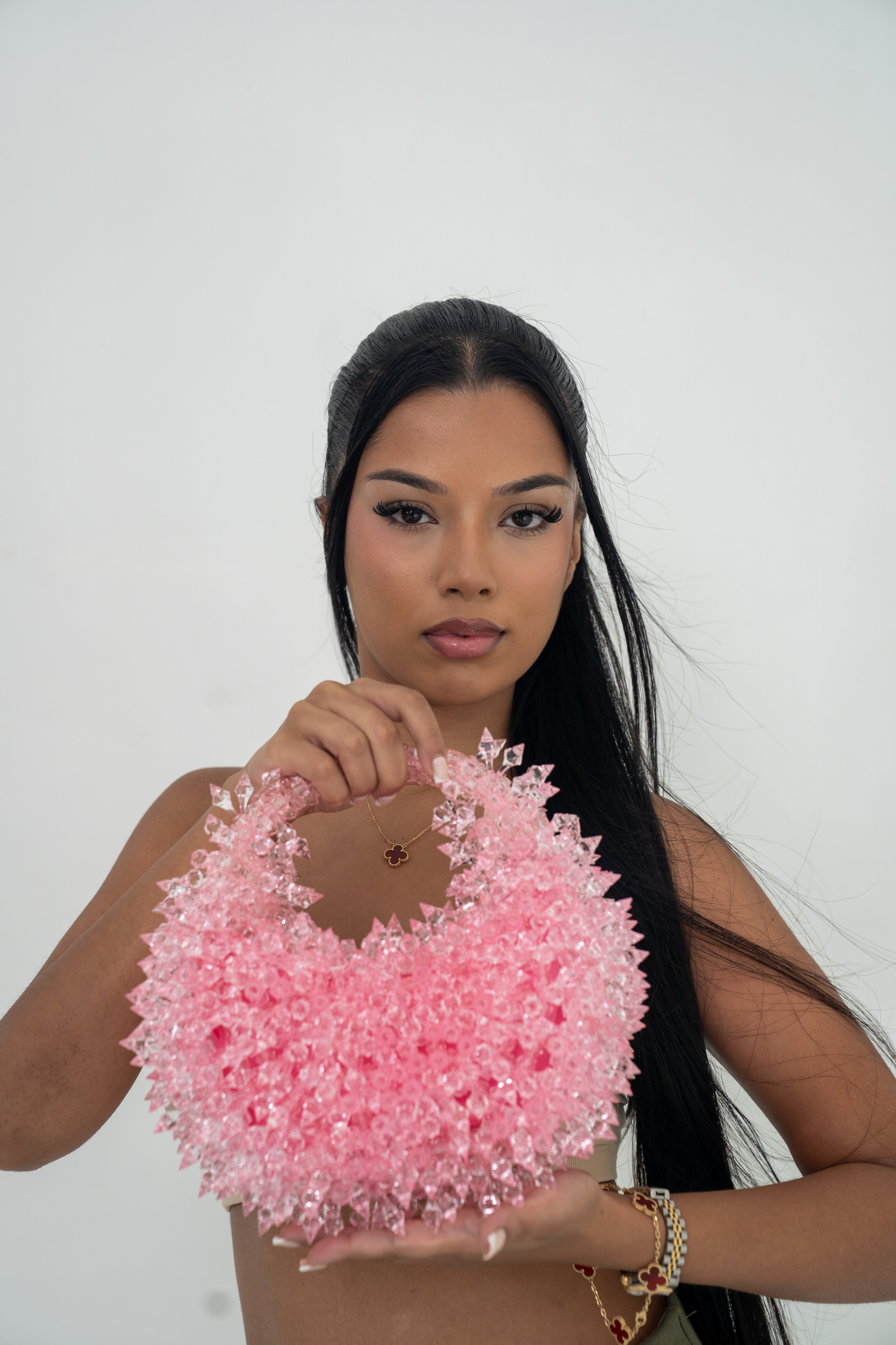A woman holding a large, textured pink circular accessory made of many small flower-like pieces, posed against a plain light gray background.