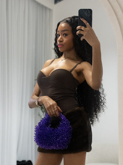 Woman taking a mirror selfie wearing a brown top and black skirt, holding a purple handbag.
