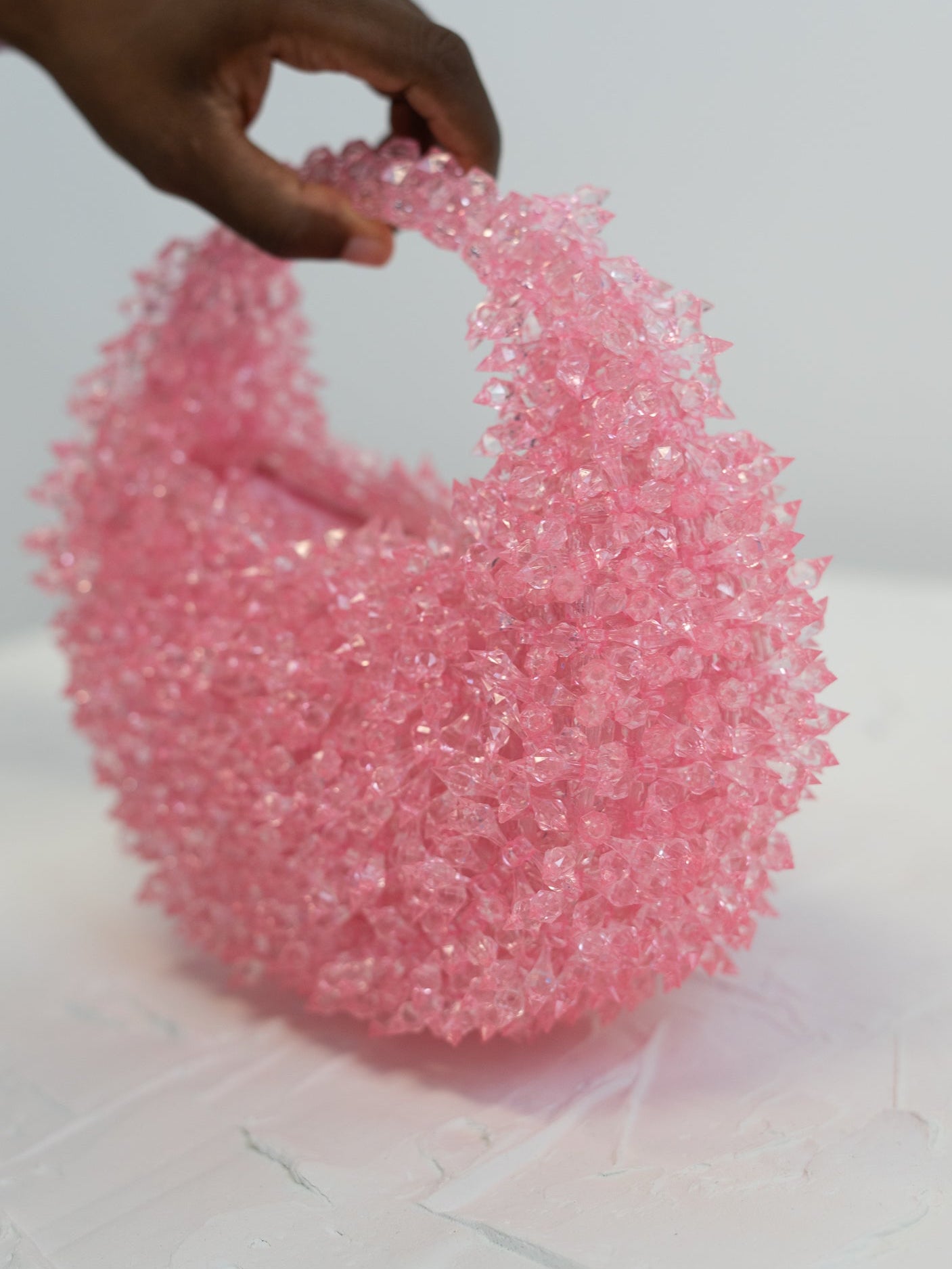 Pink beaded bag held by a hand on a white background