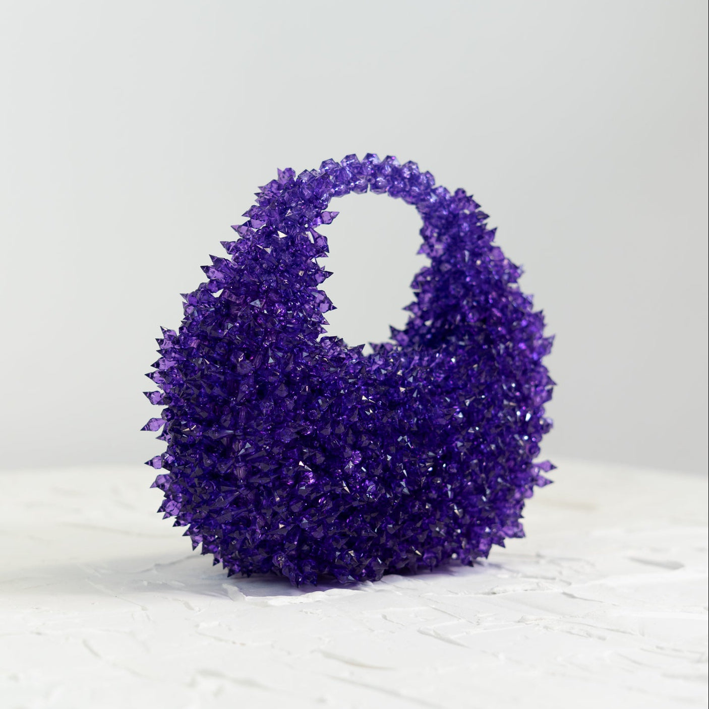 Purple textured handbag on a white surface with a light gray background[