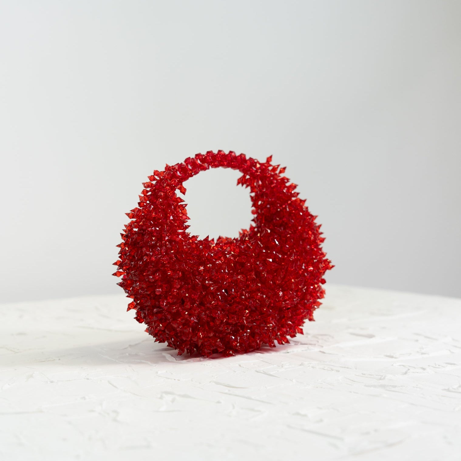 Red textured handbag on a white surface with a light gray background