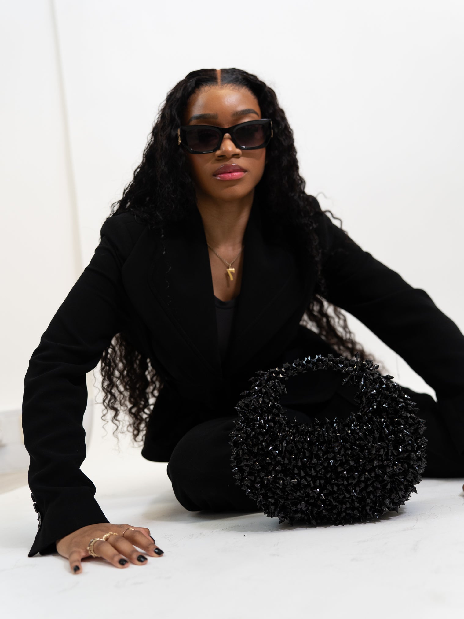Person wearing a black outfit with a textured black bag on a white background