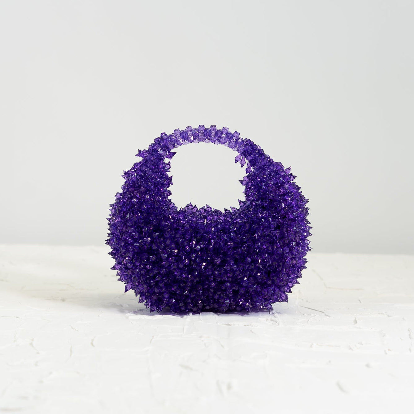 Purple textured handbag on a white surface with a light gray background